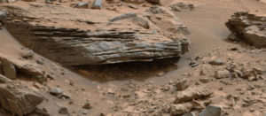 Large, worn, layered rock above grit and small rocks